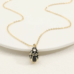 Detail of egg-shaped floral enamel pendant on a golden chain in a white ceramic tray