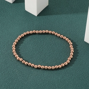 Detail view of polished 18K gold plated beaded bracelet on a dark textured background