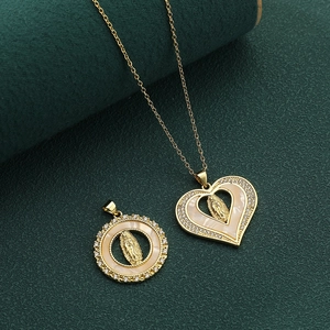 Macro view of gold Mother Mary heart pendant with white zircons on deep green backdrop