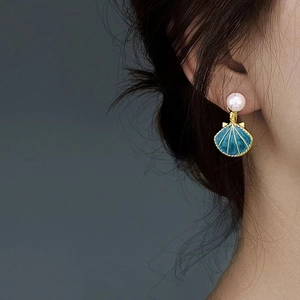 Elegant shell drop earrings with white pearls and blue scallop pendants on a model