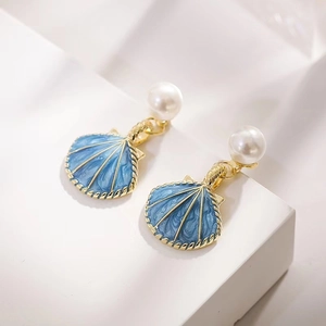 Elegant gold shell earrings with blue enamel finish and white pearl accents on display