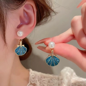 Detail of shell earring with blue enamel, gold trim and a large white imitation pearl