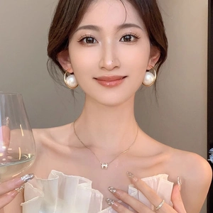 Elegant gold pearl hoop earrings and H-letter necklace set worn by a female model