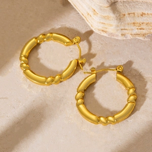 Close-up of gold geometric earrings with bamboo-style texture on a beige stone