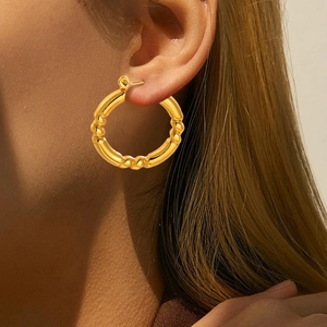 Detail of textured gold hoop earrings with a bamboo-style finish shown on a model