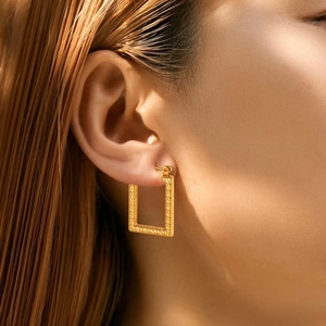 Close-up of gold geometric earrings with Greek meander pattern worn by model