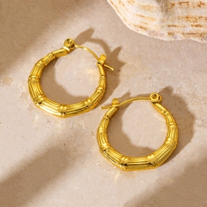 Detailed view of golden hoop earrings with bamboo texture on a marble background