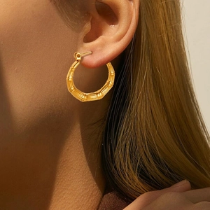 Detailed close-up of golden bamboo texture hoop earrings worn on a model's ear
