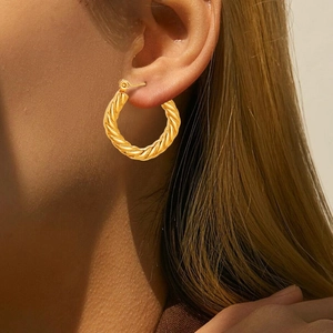 Detailed close-up of golden hoop earrings with elegant twisted rope texture on a model