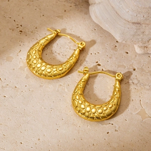Macro detail of gold U-shaped earrings featuring a vintage pebbled texture on stone surface