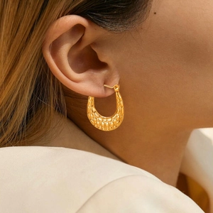Detail of chunky gold U-shaped hoop earring with textured scale pattern on model