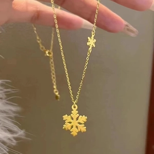Delicate gold snowflake pendant necklace on a slender O-chain held by hand