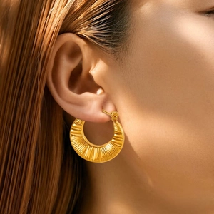 Detail of wide gold hoop earrings with vintage sunburst pleat texture on female model