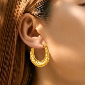 Close-up of golden U-shaped hoop earrings with vintage hammered texture on a model