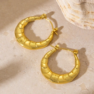Close-up of golden hoop earrings featuring a unique textured finish on a stone background
