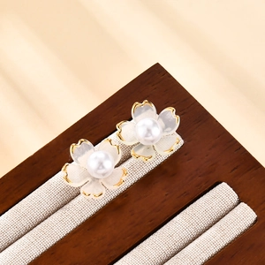 Elegantes pendientes de flor con borde dorado y perla en soporte de exhibición de madera