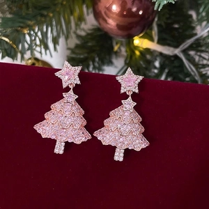 Detail of pink crystal Christmas tree earrings on red velvet with festive holiday lights