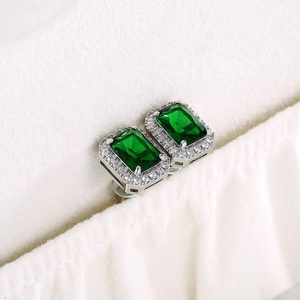 Macro detail of emerald-cut green zircon stud earrings with halo micro-pave setting