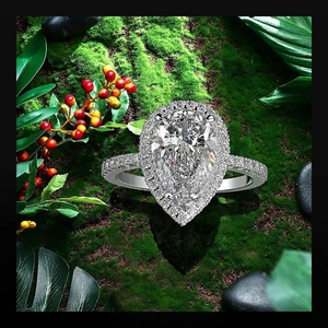 Macro detail of pear-shaped halo engagement ring on natural green moss and berry background