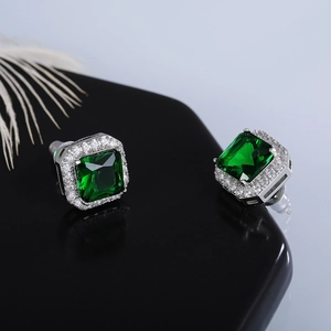Macro detail of emerald-cut green zircon stud earrings with halo diamond setting on a stand