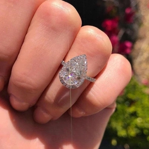 Close-up of a pear-cut diamond ring with halo setting and pavé band worn on a finger