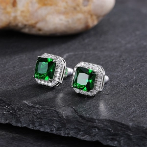 Macro detail of emerald-cut green zircon earrings with diamond halo on stone background