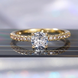 Dettaglio macro di un anello in zircone dorato con pietra centrale tonda e fascia con pavé di diamanti
