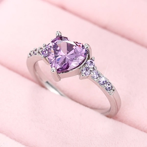 Macro detail of heart-shaped purple crystal ring with side stones on pink velvet