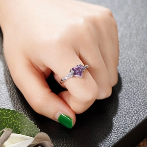 Detailed close-up of a heart-shaped purple zircon ring with silver-toned band on hand