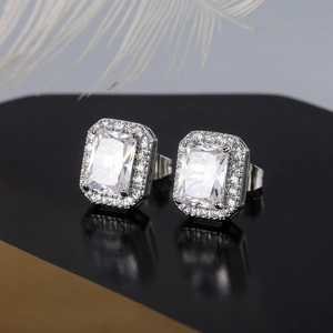 Macro view of square emerald-cut halo earrings with pavé stones on a reflective surface
