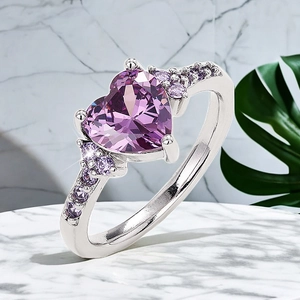 Macro detail of purple heart-shaped zircon ring on white marble and tropical leaf