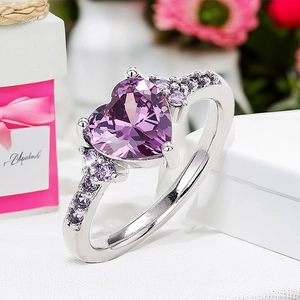 Close-up of heart-shaped purple diamond ring on white gift box with pink ribbon
