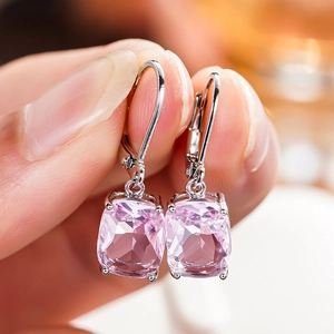 Close-up of pink cushion-cut zircon earrings held by hand to show size and silver detail