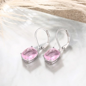 Detail of pink cushion-cut zircon earrings with silver lever-back hooks on marble surface