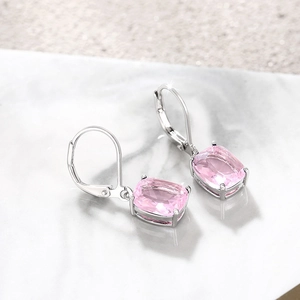 Macro shot of cushion cut pink gemstone earrings with silver lever-back closures on marble