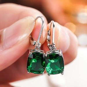 Macro shot of silver lever-back earrings with cushion-cut emerald-green gemstones