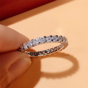Macro shot of silver eternity band featuring round-cut sparkling stones held by hand