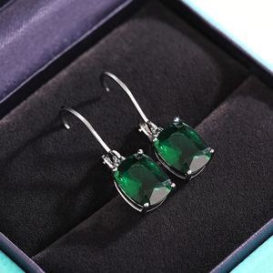Macro shot of cushion-cut emerald green gemstone earrings set in a velvet jewelry box