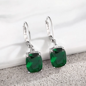 Macro shot of cushion-cut green gemstones and silver leverback ear hooks on marble