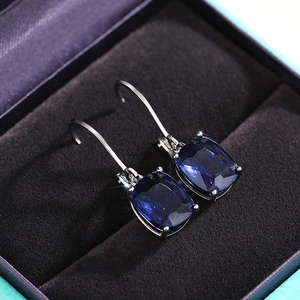 Macro shot of cushion-cut blue gemstone earrings with classic silver claw setting