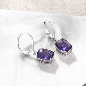 Macro detail of silver drop earrings with faceted purple rectangular stones on marble