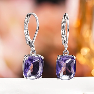 Close-up of silver drop earrings with large cushion-cut purple gemstone and claw setting