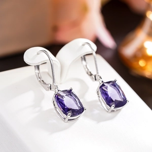 Macro view of silver drop earrings with purple cushion-cut stones on a white stand