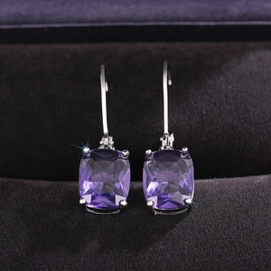 Macro shot of silver drop earrings with cushion-cut purple crystals on dark velvet