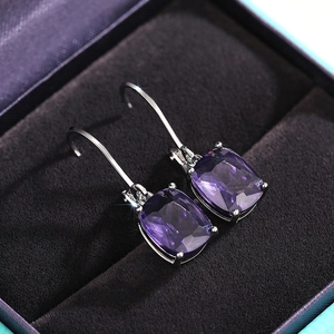 Close-up of purple cushion cut gemstones on silver hook earrings in a black jewelry box