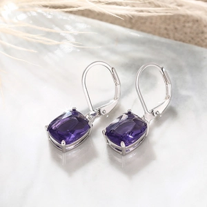 Detail of silver lever-back earrings with square purple gemstone on marble surface