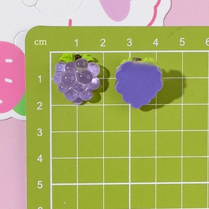 Detailed view of purple resin grape charms with size measurement on green scale board