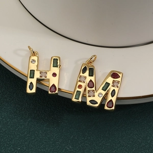 Primer plano de colgantes de letras H y M dorados con circonitas cúbicas de colores