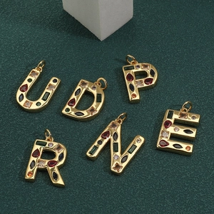 Colgantes de letras con circonitas de colores en acabado dorado sobre fondo verde