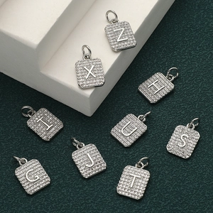 Macro shot of silver square alphabet pendants with cubic zirconia on a green background